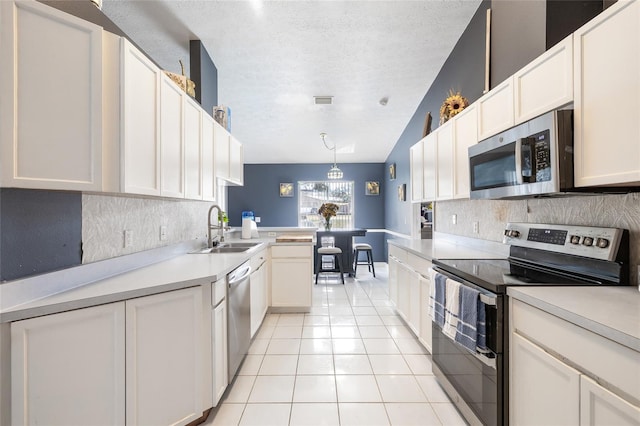 kitchen with white cabinets, appliances with stainless steel finishes, sink, and vaulted ceiling