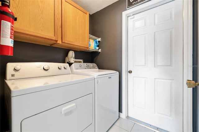 laundry room featuring a textured ceiling, separate washer and dryer, cabinets, and light tile patterned floors