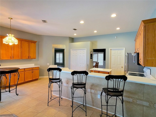 kitchen with pendant lighting, white stove, stainless steel fridge, light tile patterned floors, and a breakfast bar area