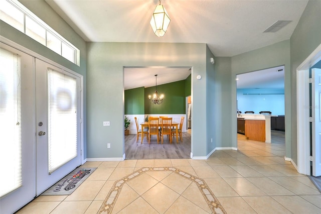 entrance foyer with a chandelier, tile patterned flooring, a healthy amount of sunlight, and vaulted ceiling