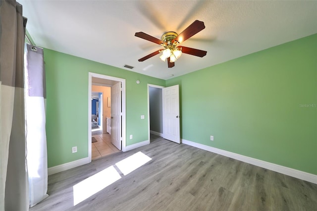 unfurnished bedroom featuring a textured ceiling, ensuite bath, light hardwood / wood-style flooring, and ceiling fan