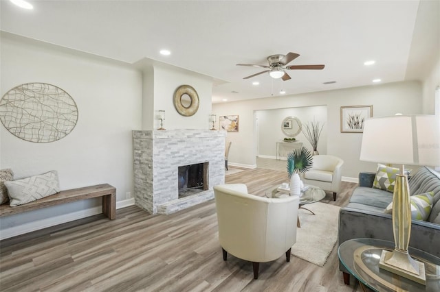 living room featuring a stone fireplace, ceiling fan, and hardwood / wood-style floors