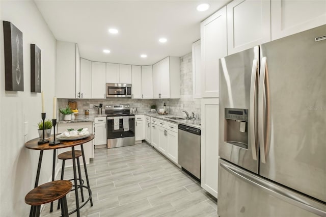 kitchen with backsplash, sink, light stone countertops, white cabinetry, and stainless steel appliances