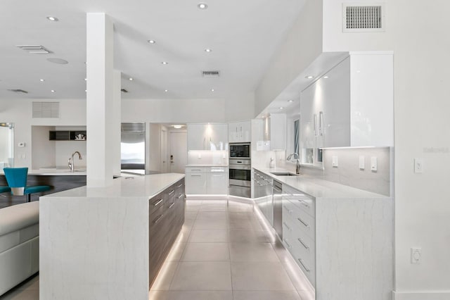 kitchen with sink, light tile patterned floors, built in appliances, white cabinets, and a large island