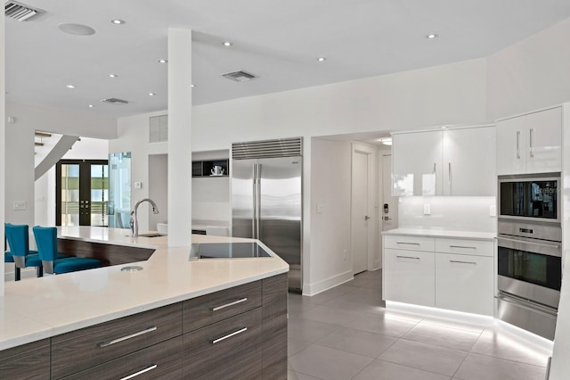 kitchen featuring appliances with stainless steel finishes, dark brown cabinetry, sink, white cabinetry, and light tile patterned flooring