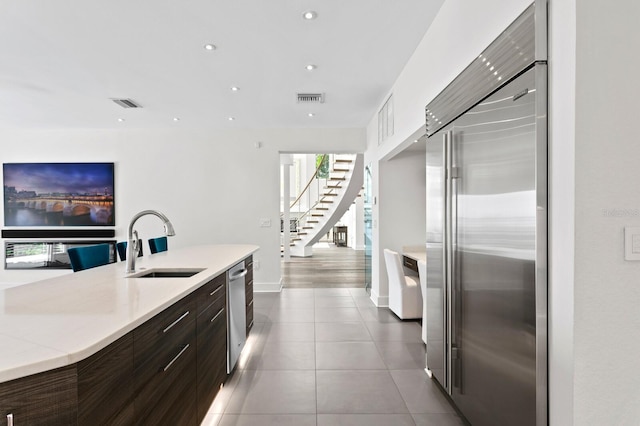 kitchen featuring dark brown cabinets, sink, light tile patterned floors, and stainless steel appliances