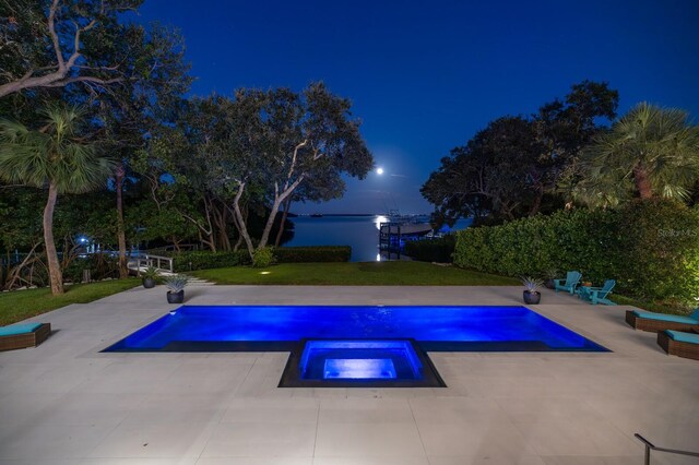 pool at twilight featuring a lawn, a patio area, and an in ground hot tub