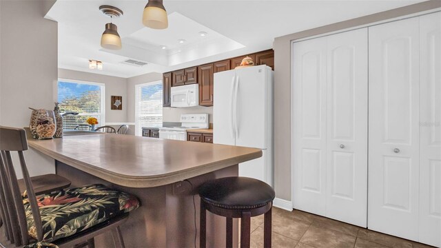 kitchen featuring white appliances, a breakfast bar, kitchen peninsula, tile patterned floors, and a raised ceiling