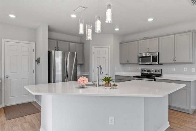 kitchen with light hardwood / wood-style floors, a center island with sink, and appliances with stainless steel finishes