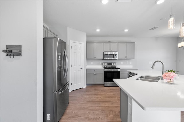 kitchen featuring sink, appliances with stainless steel finishes, hanging light fixtures, hardwood / wood-style floors, and gray cabinetry