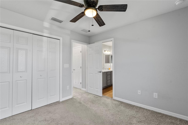 unfurnished bedroom featuring ceiling fan, ensuite bath, a closet, and light colored carpet