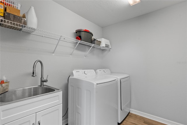 clothes washing area with cabinets, a textured ceiling, sink, washing machine and clothes dryer, and light wood-type flooring