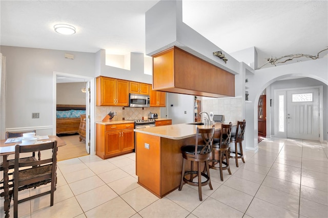 kitchen featuring vaulted ceiling, light tile patterned floors, a breakfast bar, and appliances with stainless steel finishes