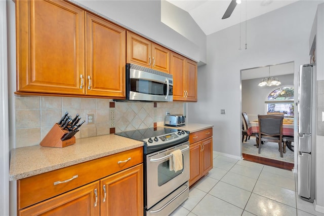 kitchen featuring light tile patterned flooring, appliances with stainless steel finishes, light stone countertops, lofted ceiling, and ceiling fan with notable chandelier