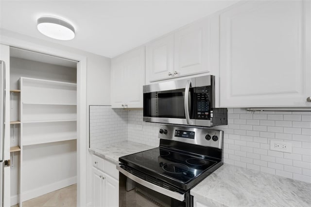 kitchen with stainless steel appliances, light tile patterned floors, light stone counters, decorative backsplash, and white cabinets