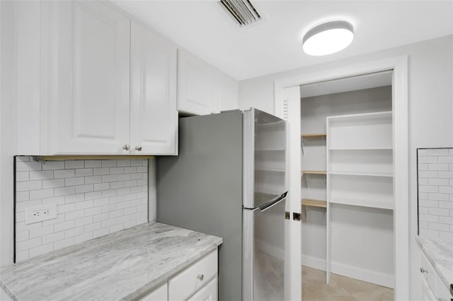 kitchen with decorative backsplash, stainless steel fridge, white cabinets, and light stone countertops