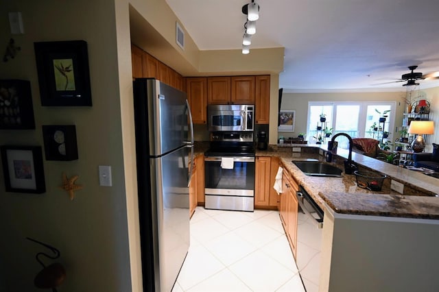 kitchen with appliances with stainless steel finishes, dark stone counters, ceiling fan, sink, and light tile patterned floors