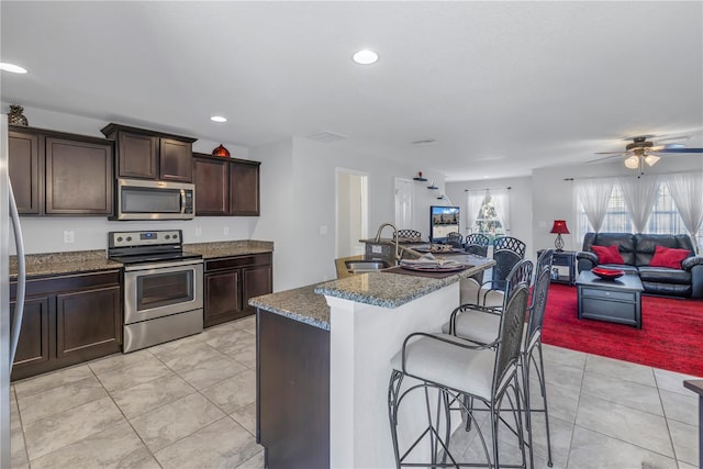 kitchen with a center island with sink, a kitchen breakfast bar, sink, ceiling fan, and stainless steel appliances