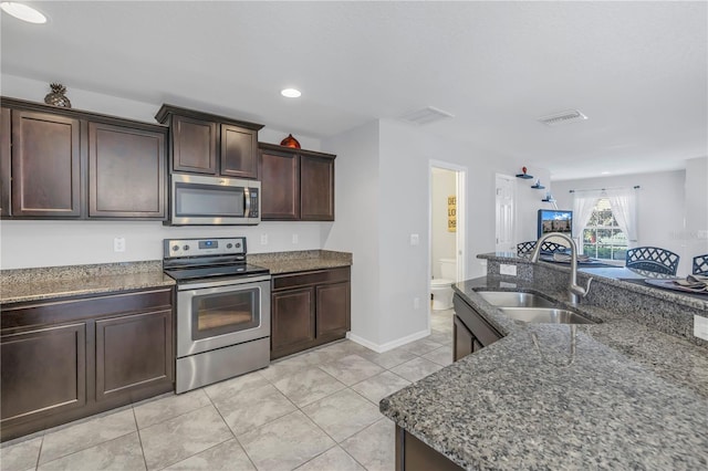 kitchen with dark stone counters, sink, light tile patterned flooring, dark brown cabinetry, and stainless steel appliances