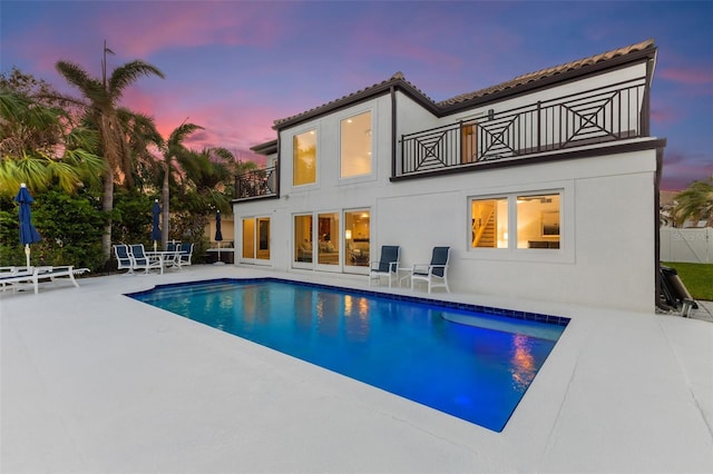 back house at dusk featuring a fenced in pool, a patio area, and a balcony