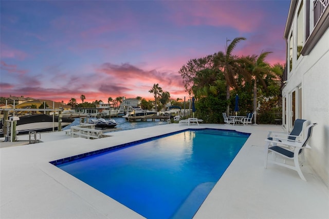 pool at dusk featuring a boat dock, a patio, and a water view