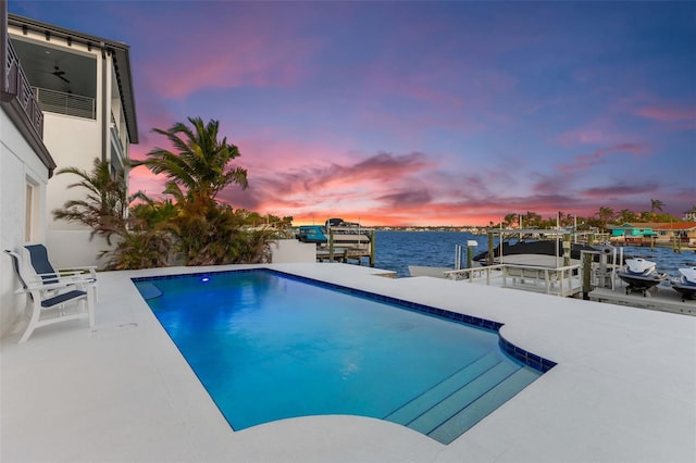 pool at dusk with a water view and a boat dock