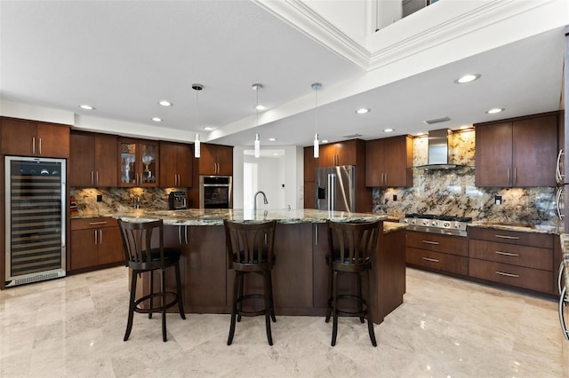 kitchen with wall chimney exhaust hood, stainless steel appliances, beverage cooler, a spacious island, and decorative light fixtures