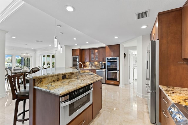 kitchen featuring decorative backsplash, stainless steel appliances, sink, a large island with sink, and hanging light fixtures