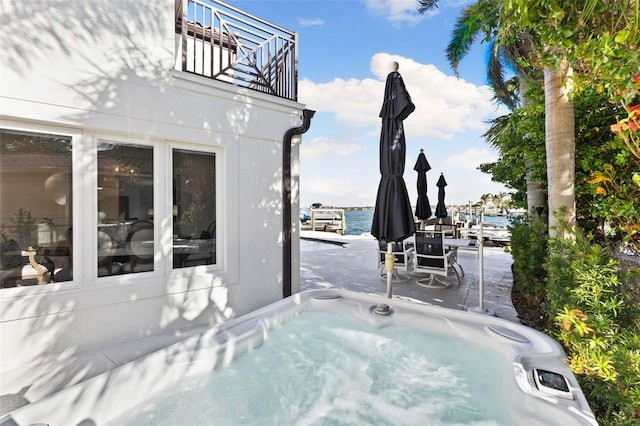 view of patio with a balcony, a hot tub, and a water view