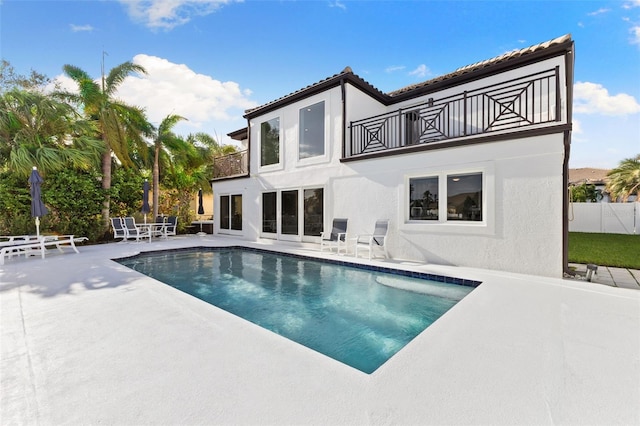 rear view of property with a fenced in pool, a balcony, and a patio