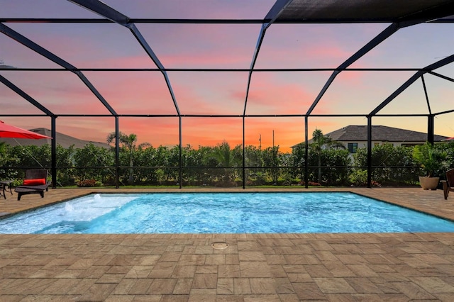 pool at dusk featuring a lanai and a patio