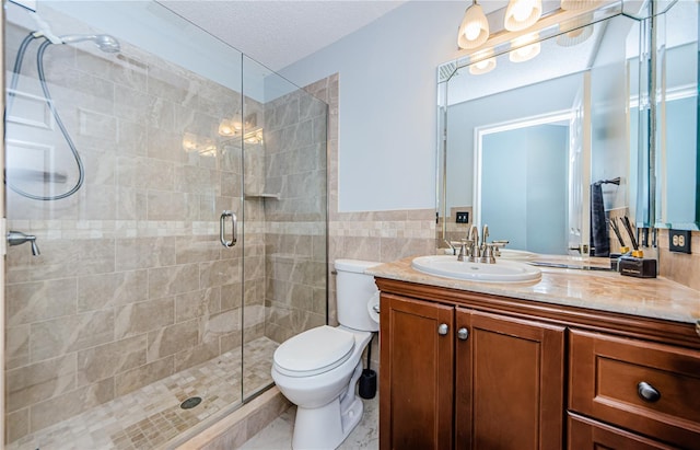 bathroom with a textured ceiling, vanity, a shower with shower door, toilet, and tile walls