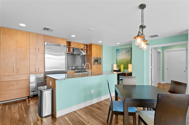 kitchen featuring built in appliances, a kitchen island with sink, dark hardwood / wood-style flooring, and pendant lighting