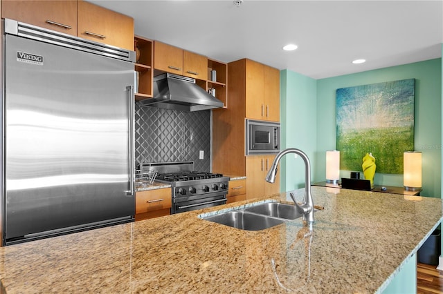 kitchen featuring decorative backsplash, light stone counters, sink, wood-type flooring, and built in appliances