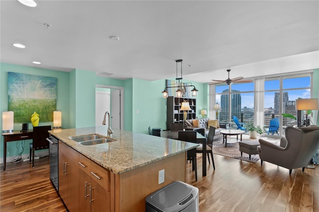 kitchen with light stone countertops, a kitchen island with sink, sink, dark hardwood / wood-style floors, and hanging light fixtures