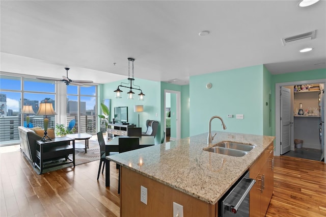 kitchen with light stone counters, sink, pendant lighting, a center island with sink, and light hardwood / wood-style floors