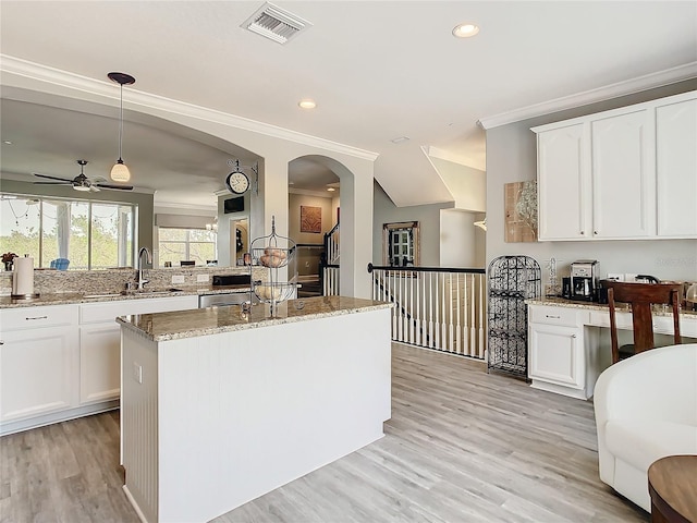 kitchen with light hardwood / wood-style floors, white cabinetry, light stone counters, decorative light fixtures, and a kitchen island