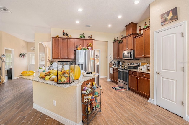 kitchen featuring tasteful backsplash, light wood-type flooring, appliances with stainless steel finishes, and a kitchen bar