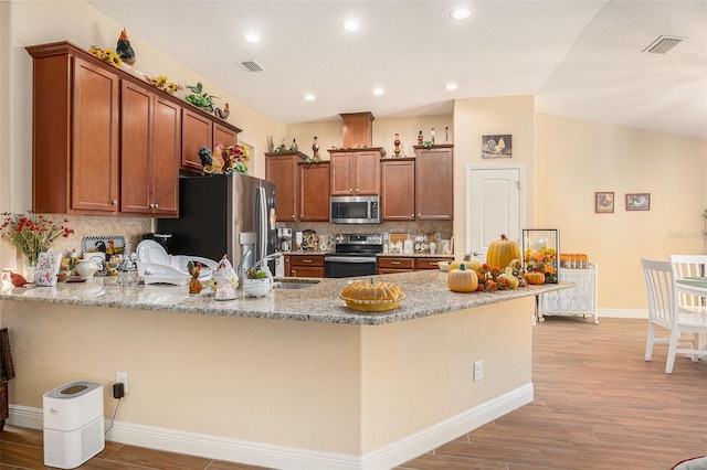 kitchen featuring kitchen peninsula, stainless steel appliances, light wood-type flooring, and backsplash