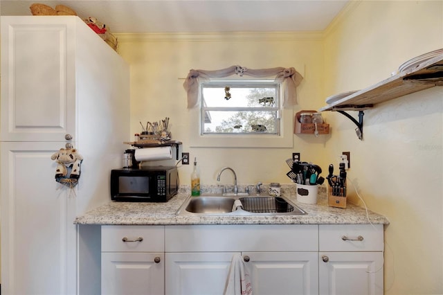 kitchen with white cabinets, light stone counters, ornamental molding, and sink