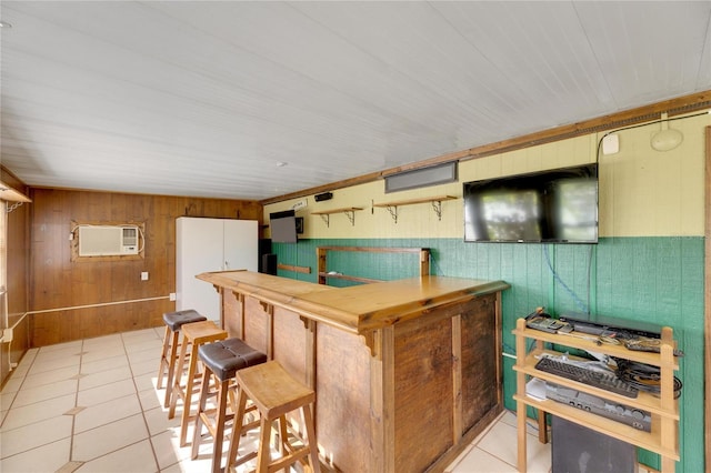 kitchen featuring light tile patterned floors, an AC wall unit, a kitchen breakfast bar, and wood walls