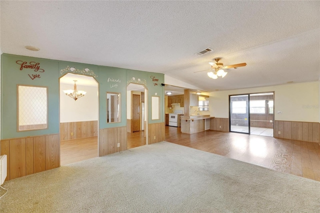 unfurnished living room with a textured ceiling, ceiling fan with notable chandelier, vaulted ceiling, and hardwood / wood-style flooring