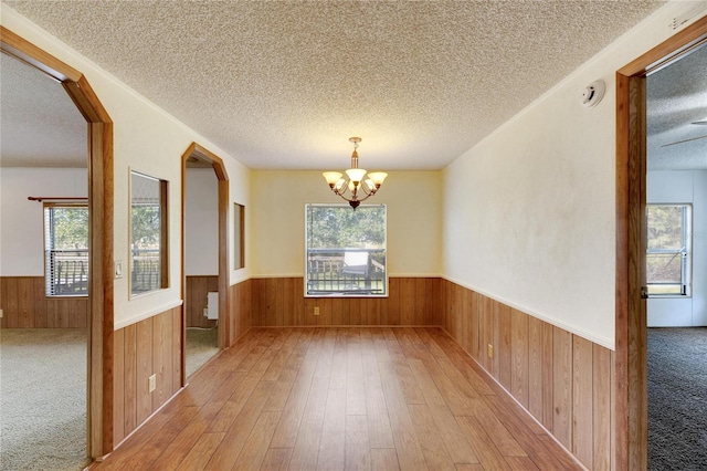 unfurnished dining area featuring a textured ceiling, light hardwood / wood-style floors, and wood walls