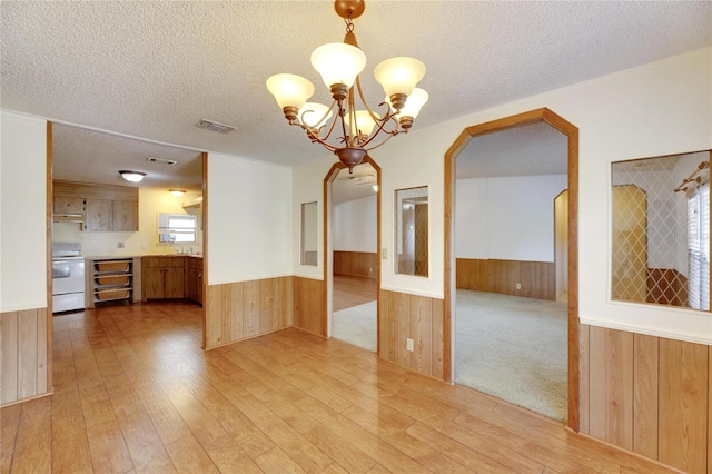 spare room featuring a chandelier, wood walls, light hardwood / wood-style floors, and a textured ceiling