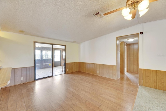 empty room with ceiling fan, light hardwood / wood-style floors, a textured ceiling, and wooden walls