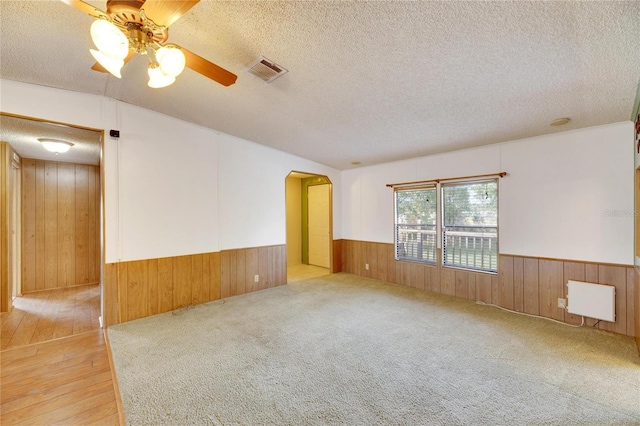 spare room with a textured ceiling, light hardwood / wood-style flooring, ceiling fan, and wooden walls