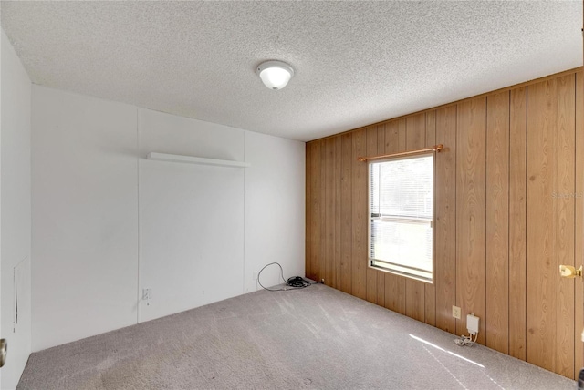 empty room featuring carpet flooring, wooden walls, and a textured ceiling