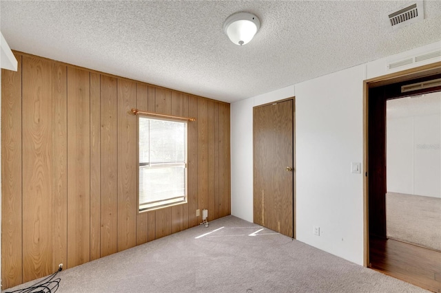 unfurnished bedroom featuring carpet flooring, a textured ceiling, and wood walls