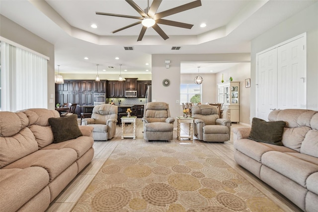 living room featuring light wood-type flooring, a raised ceiling, and ceiling fan