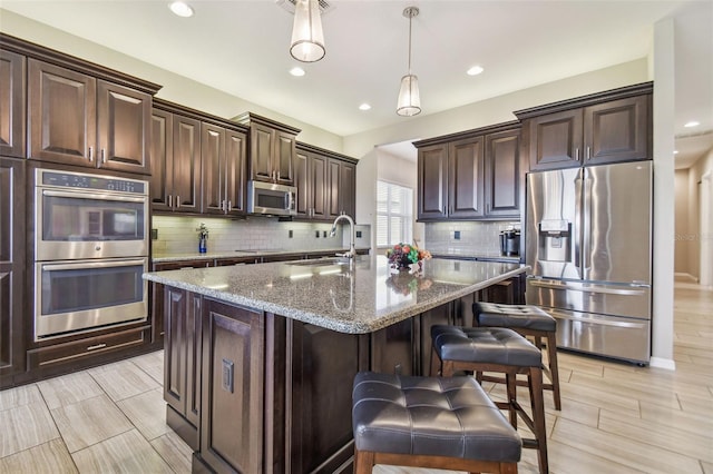 kitchen featuring sink, stainless steel appliances, stone countertops, dark brown cabinets, and a center island with sink